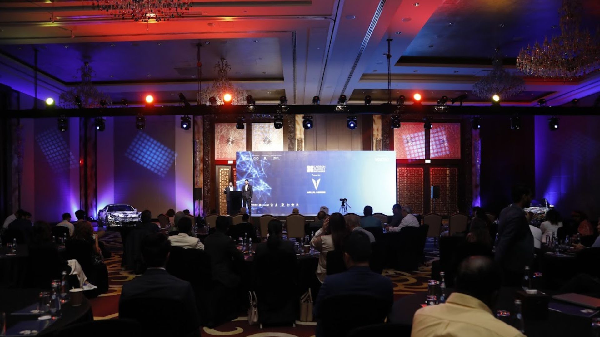 A plenary session under stage lighting in a hotel ballroom